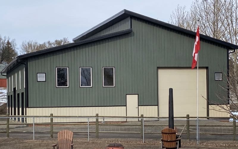 A dark sage post-frame lifestyle & hobby storage building with eight overhead doors, wainscoting and soffits