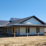 A white white post-frame custom residential build with soffits, open lean-to porch, and overhead doors