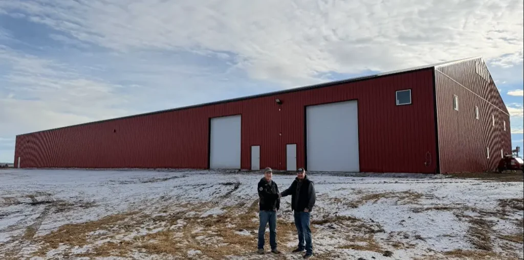 A bright red post-frame equestrian barn with overhead doors and a black roof