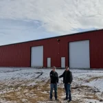 A bright red post-frame equestrian barn with overhead doors and a black roof