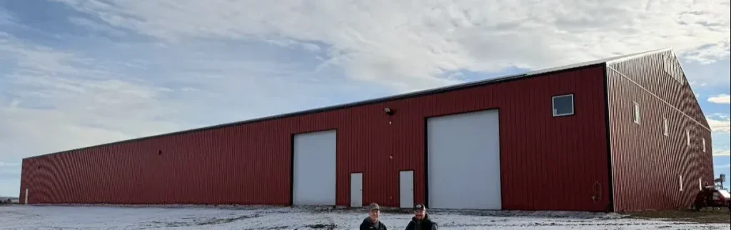 A bright red post-frame equestrian barn with overhead doors and a black roof