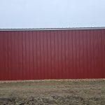 A dark red post-frame equestrian barn with sliding doors