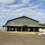 A dark sage post-frame accessory building with an agricultural shop and barn