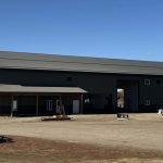 A dark sage post-frame accessory building with an agricultural shop and barn