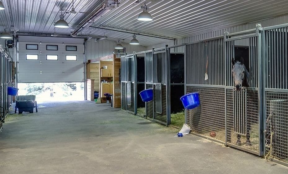 A post-frame equestrian barn with overhead doors and white walls