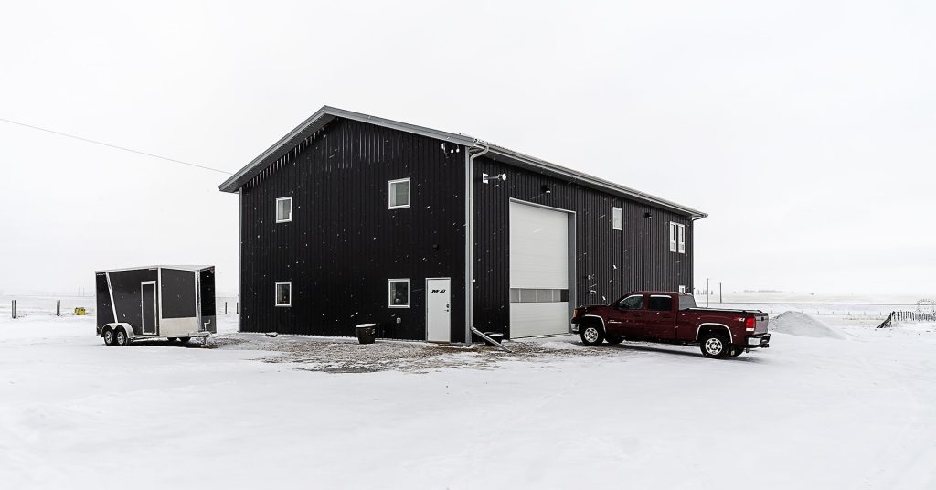 A black post-frame lifestyle & hobby shop with soffits and a overhead door