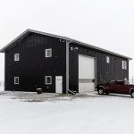 A black post-frame lifestyle & hobby shop with soffits and a overhead door