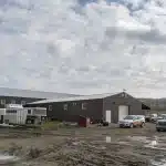 A coffee brown post-frame equestrian riding arena with overhead doors and an open lean-to