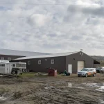 A coffee brown post-frame equestrian riding arena with overhead doors and an open lean-to