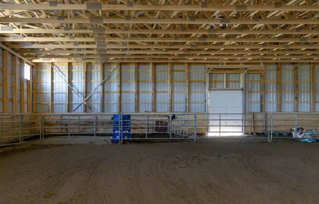 A coffee brown post-frame equestrian riding arena with overhead doors and an open lean-to