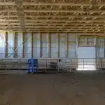 A coffee brown post-frame equestrian riding arena with overhead doors and an open lean-to