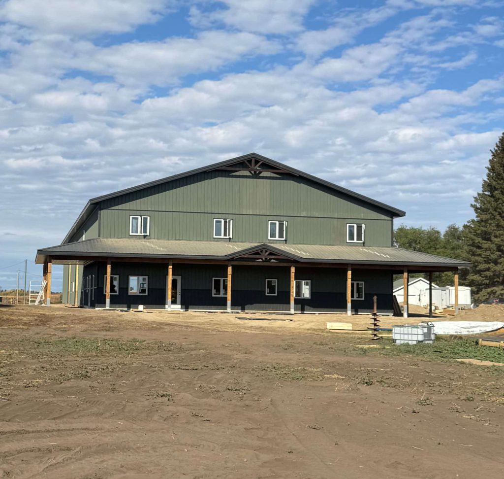 A dark sage post-frame accessory building with an agricultural shop and barn