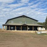 A dark sage post-frame accessory building with an agricultural shop and barn