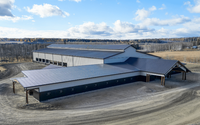 A stone grey, post-frame equestrian Riding Arena with kick wall, open/closed lean-tos, and soffits