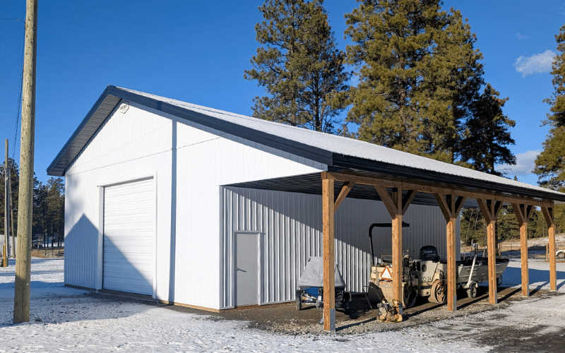 A bright white post-frame agricultural shop with ope lean-to, overhead door, and soffits
