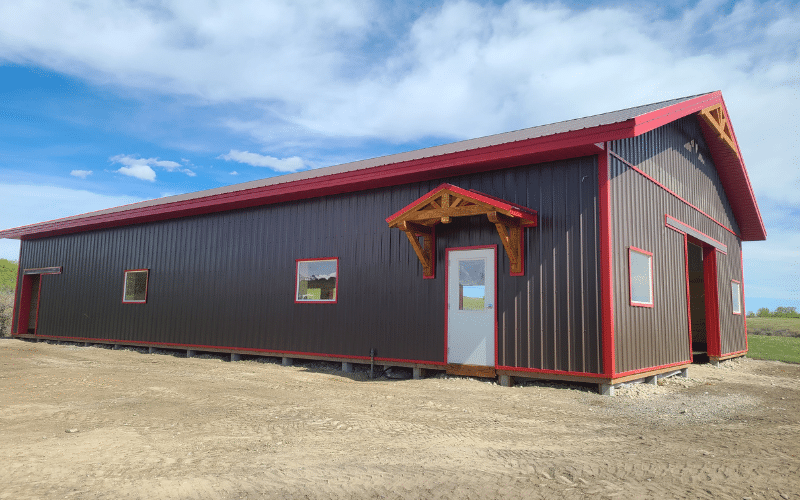 A coffee brown post-frame equestrian barn with overhead doors, soffits, and timber accents