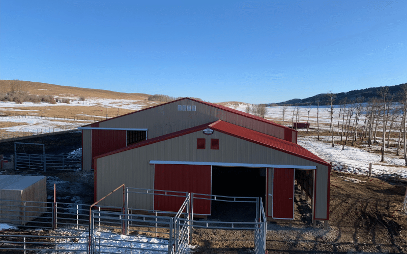 A tan post-frame equestrian barn with sliding and overhead doors