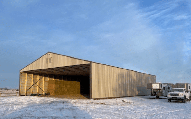 A stone grey post-frame equestrian hay shed
