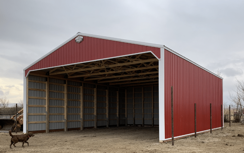 A dark red post-frame equestrian hay shed