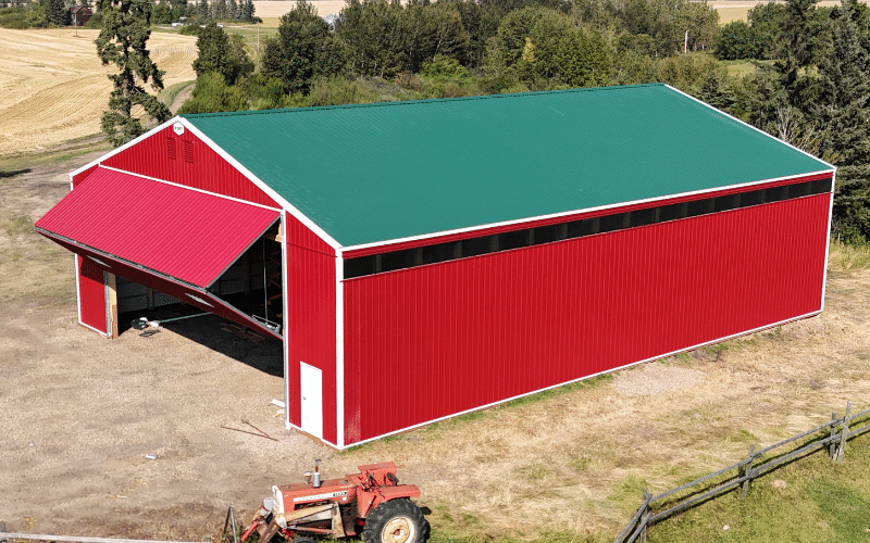 A dark red post-frame agricultural storage building with a melchers green roof