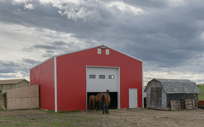 A post frame bright red equestrian barn with a overhead door