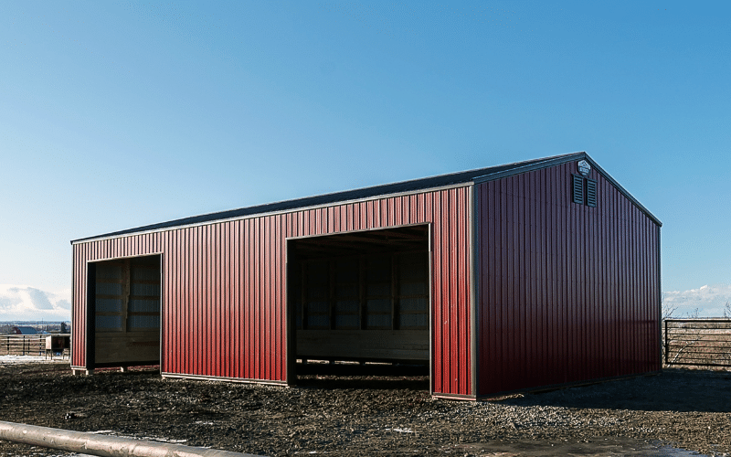 A dark red post-frame equestrian livestock shelter with two overhead doors