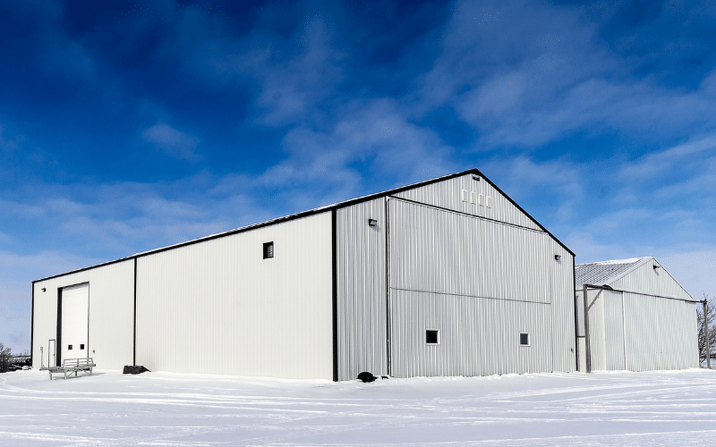 A white white post-frame agricultural storage building with bifold and overhead doors