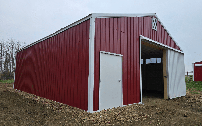 A dark red post-frame equestrian barn with sliding doors