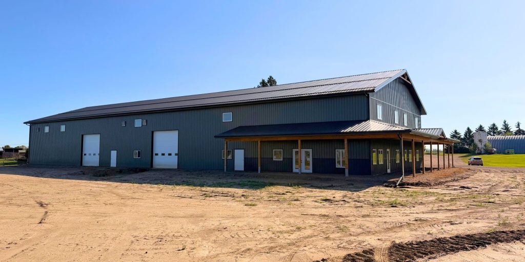 A dark sage post-frame accessory building with an agricultural shop and barn