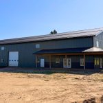 A dark sage post-frame accessory building with an agricultural shop and barn