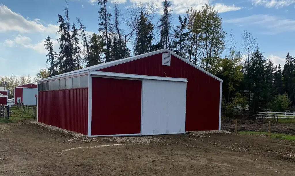 A dark red post-frame equestrian barn with sliding doors