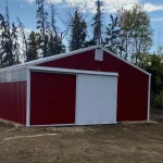A dark red post-frame equestrian barn with sliding doors