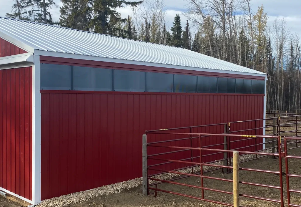 A dark red post-frame equestrian barn with sliding doors