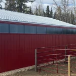 A dark red post-frame equestrian barn with sliding doors