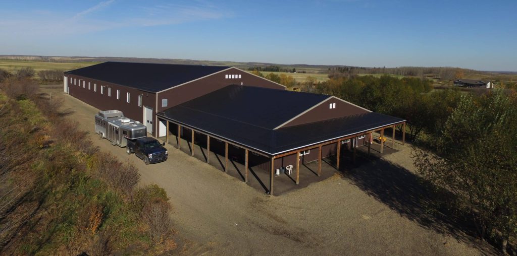 A coffee brown post-frame equestrian riding arena with open lean-to front porch
