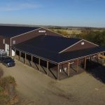 A coffee brown post-frame equestrian riding arena with open lean-to front porch