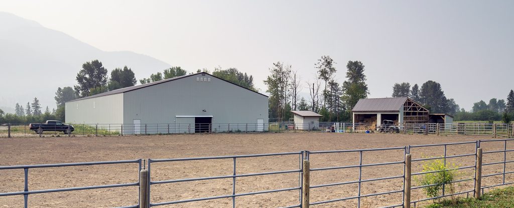 A bone white post-frame equestrian riding arena with sliding and overhead doors