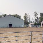 A bone white post-frame equestrian riding arena with sliding and overhead doors