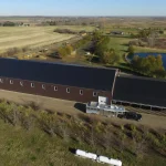 A coffee brown post-frame equestrian riding arena with open lean-to front porch