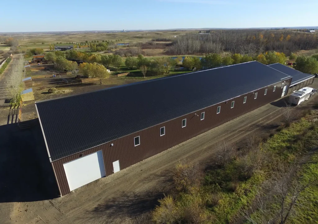 A coffee brown post-frame equestrian riding arena with open lean-to front porch