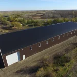 A coffee brown post-frame equestrian riding arena with open lean-to front porch