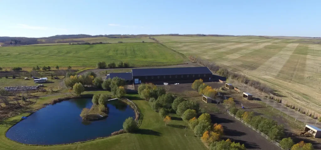 A coffee brown post-frame equestrian riding arena with open lean-to front porch