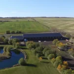 A coffee brown post-frame equestrian riding arena with open lean-to front porch