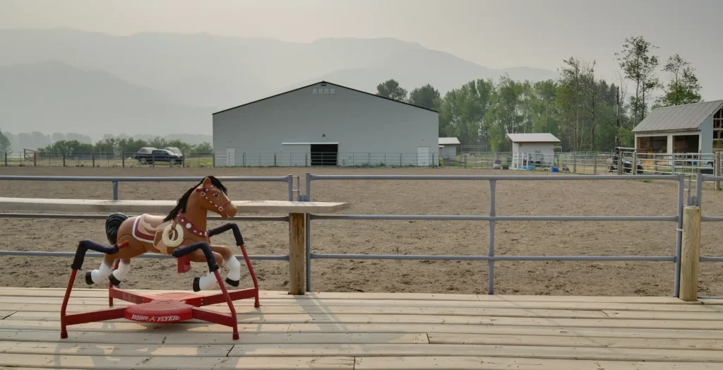 A bone white post-frame equestrian riding arena with sliding and overhead doors