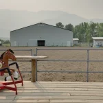 A bone white post-frame equestrian riding arena with sliding and overhead doors