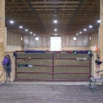 A bone white post-frame equestrian riding arena with sliding and overhead doors