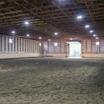 A bone white post-frame equestrian riding arena with sliding and overhead doors