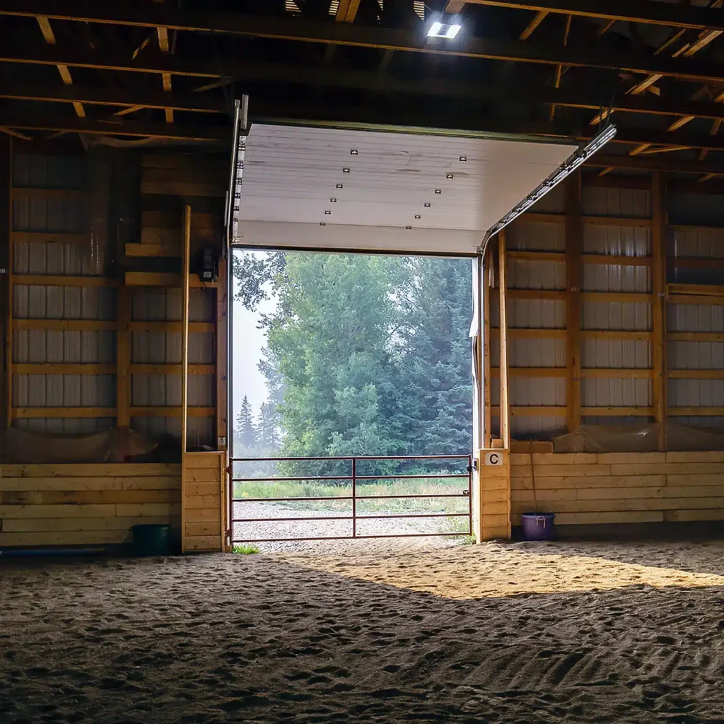 A bone white post-frame equestrian riding arena with sliding and overhead doors