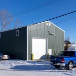 A dark sage commercial shop with a front porch and open lean-to