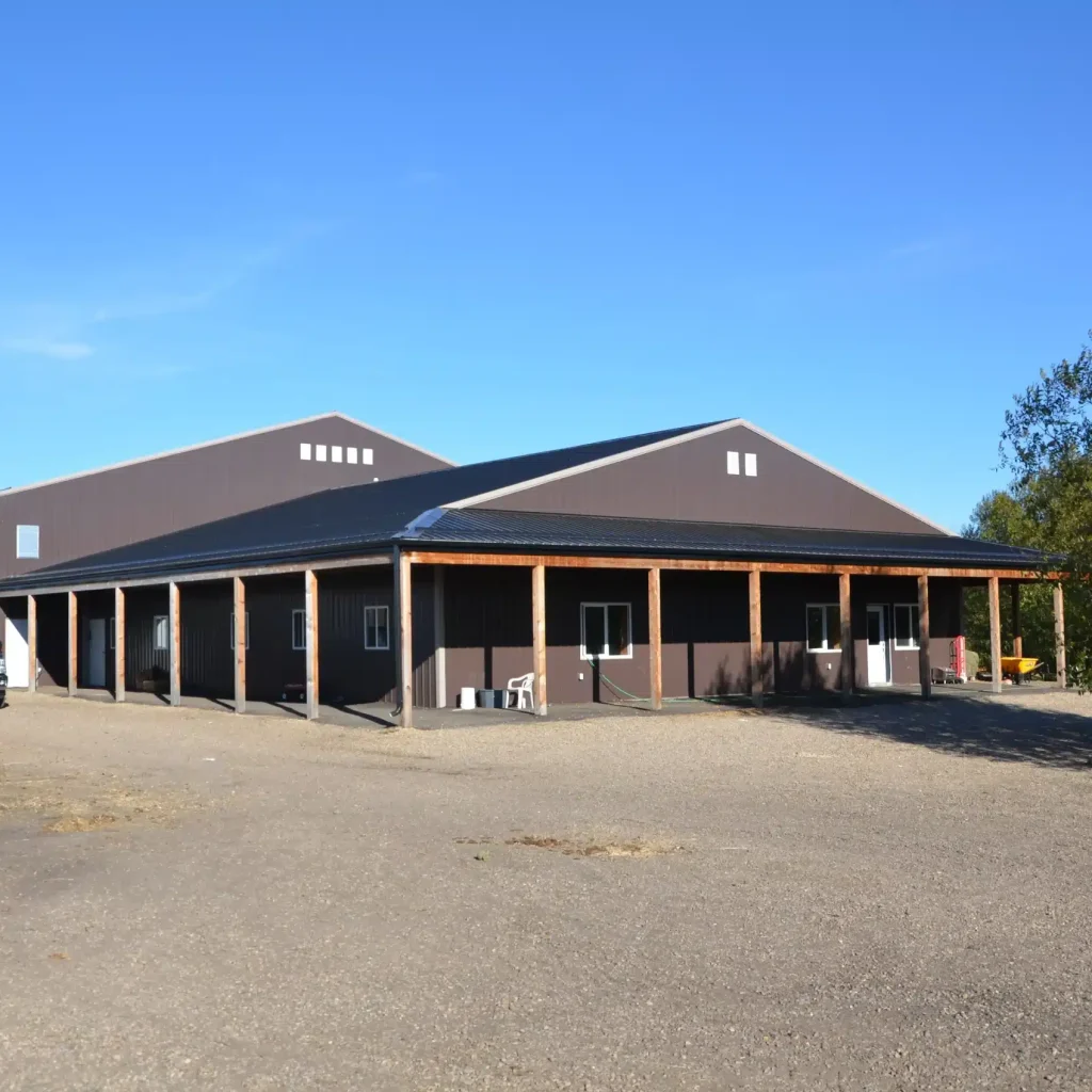A coffee brown post-frame equestrian riding arena with open lean-to front porch